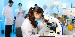 Junge Wissenschaftlerin untersucht Proben unter einem Mikroskop in einem modernen Labor.